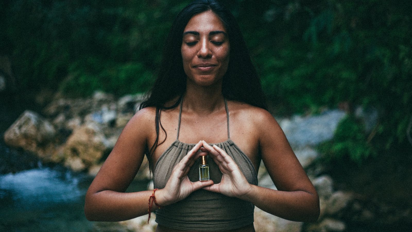 Moana with closed eyes, holding a small bottle of oil between her hands in a mudra